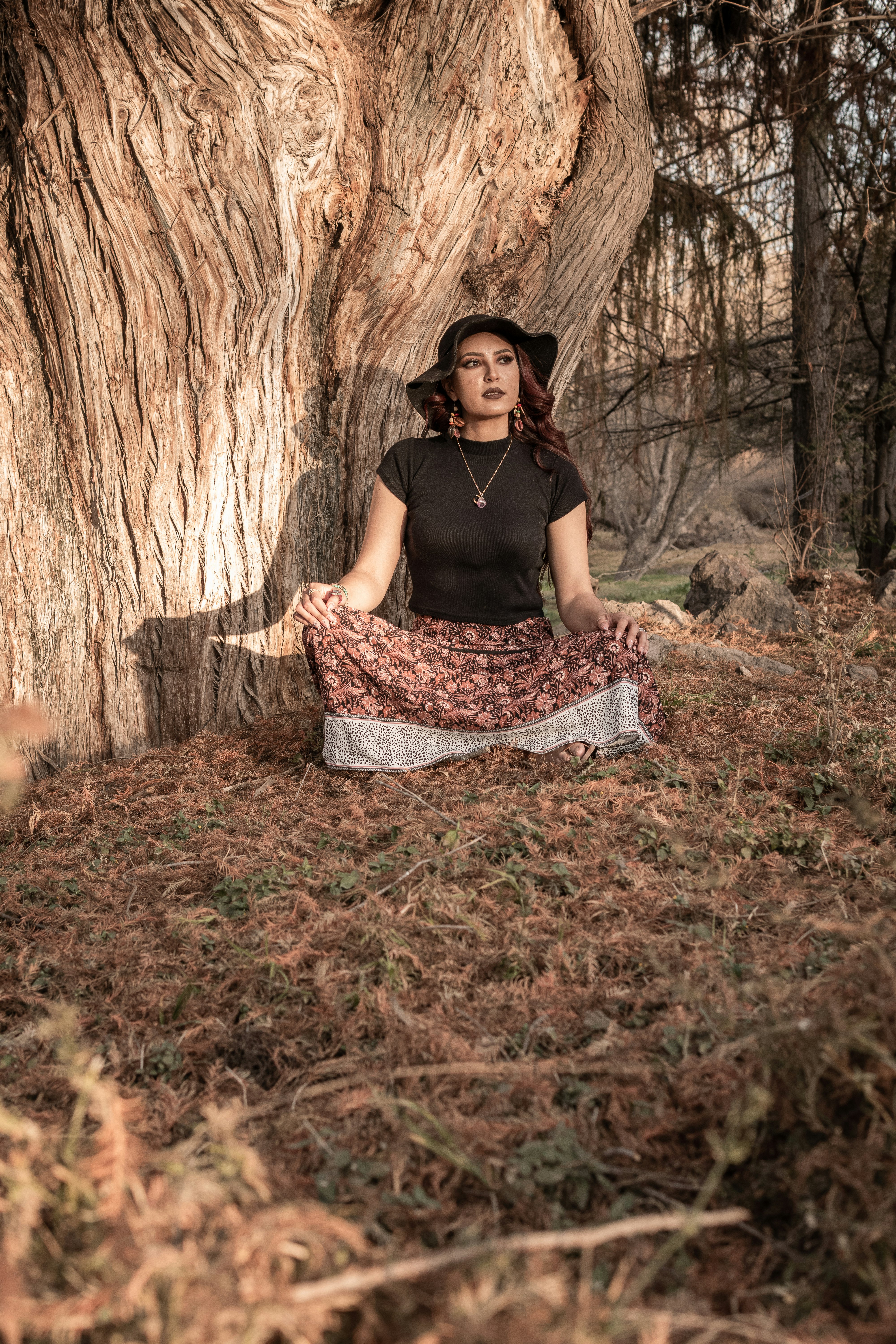 woman in black tank top and white and black skirt sitting on brown dried leaves during